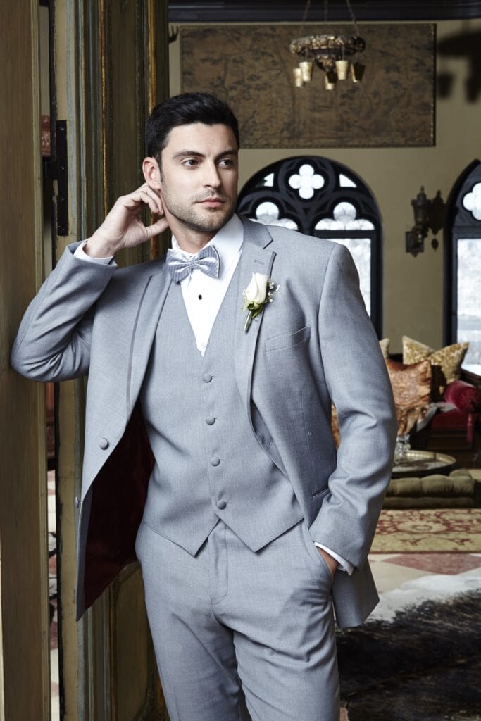 A heather grey three piece tuxedo with a boutonniere, in a ballroom