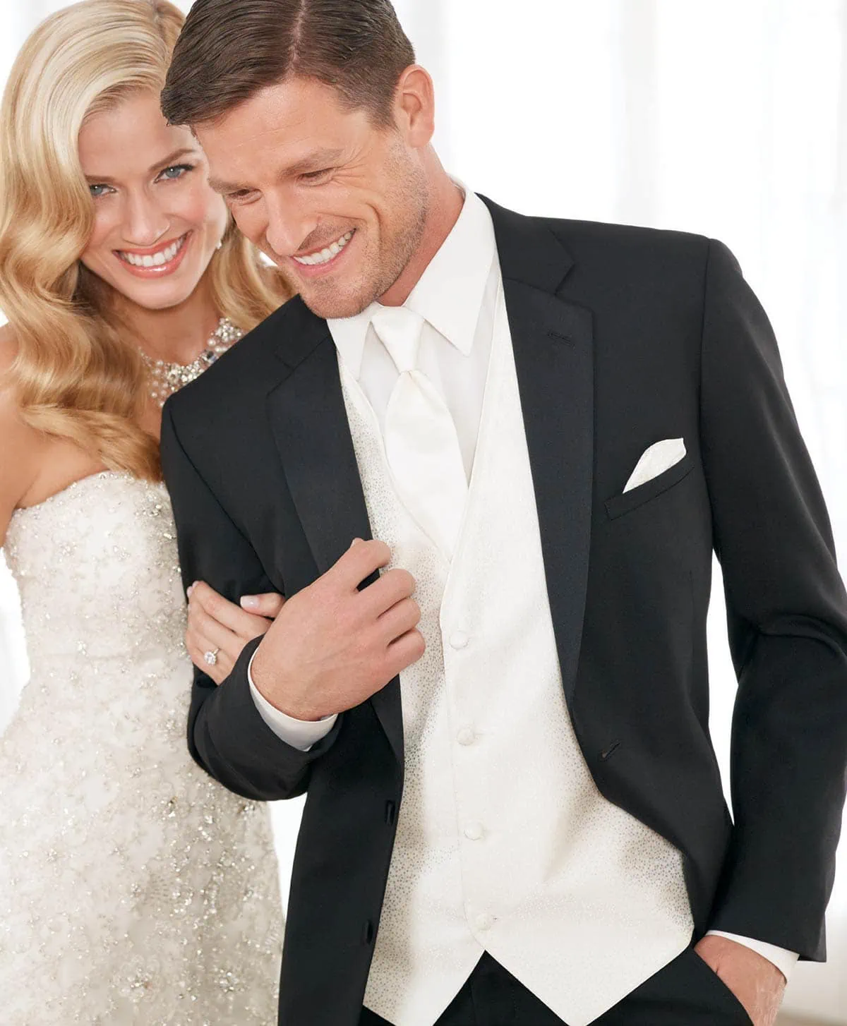Two models pose for a photo, they appear to be a couple and the man is wearing a black Modern Essential tuxedo with white accessories.