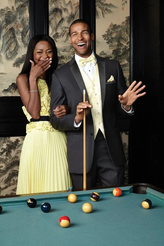A young man and his date are having a good time at a pool table, the man is dressed in the heritage tuxedo.